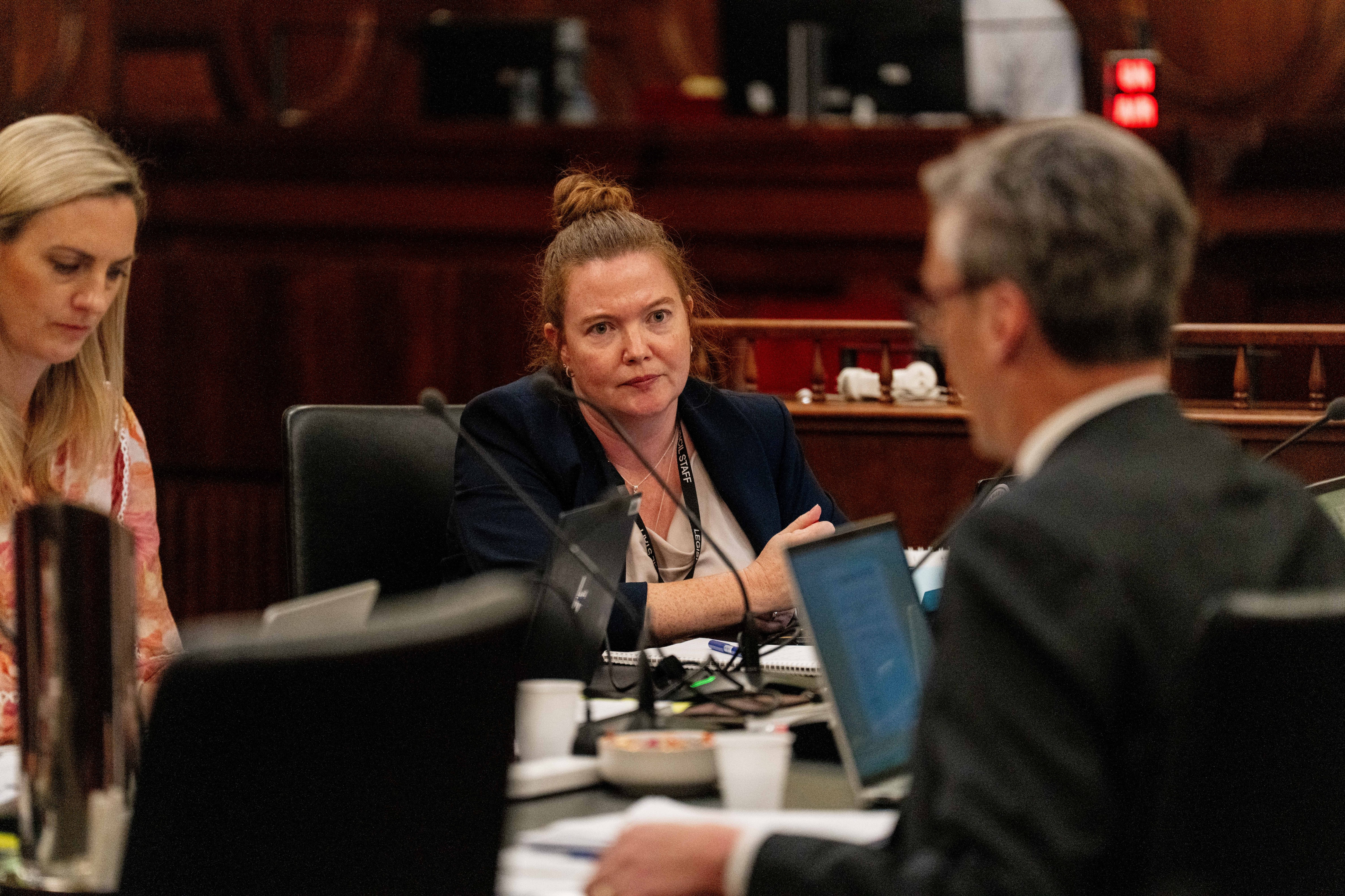 Woman looking sitting at a board room table looking at a man opposite her