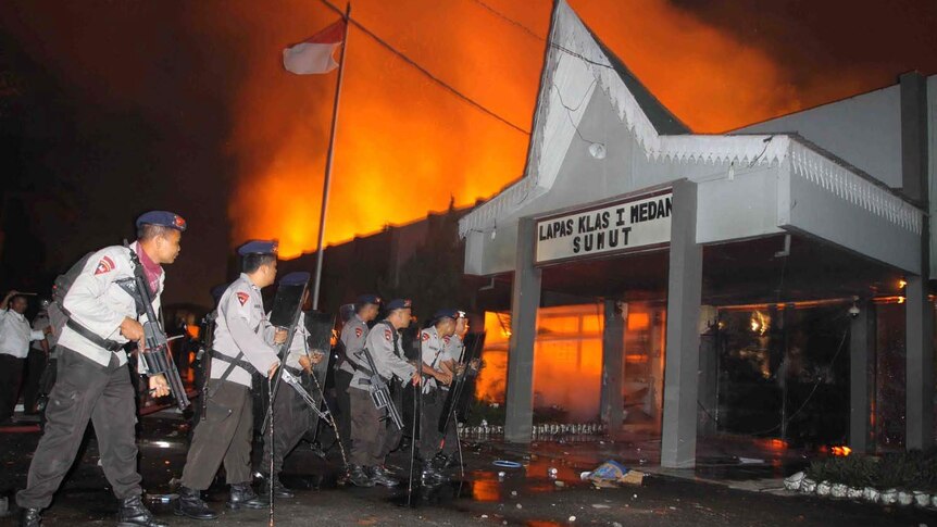 Police secure the entrance of a burning prison
