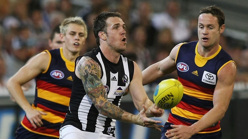 A Collingwood footballer handballs, surrounded by Adelaide players.