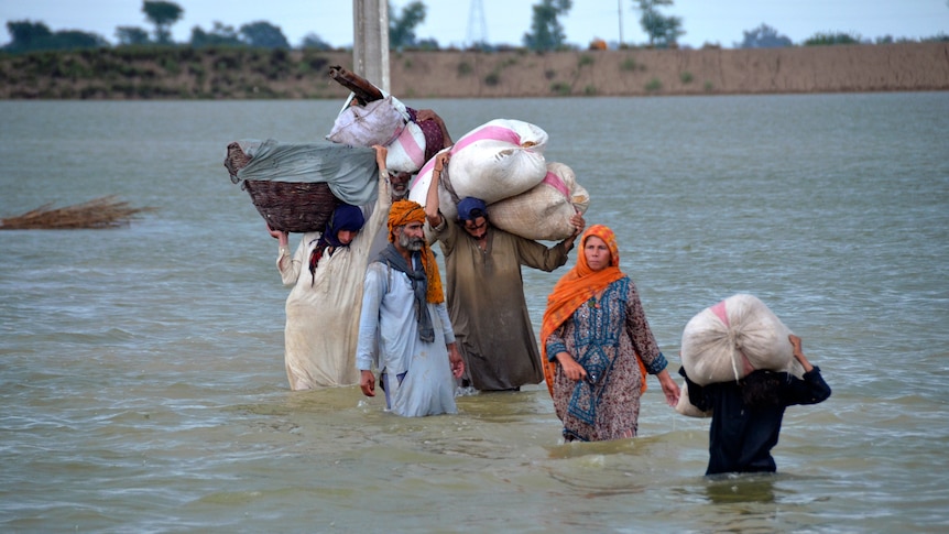 A displaced family wades through a flooded area with belongings in bags above their heads.