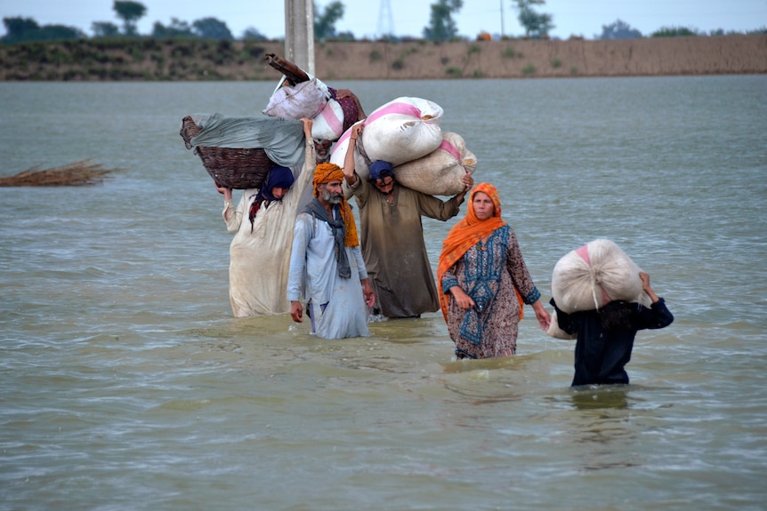 A displaced family wades through a flooded area with belongings in bags above their heads.