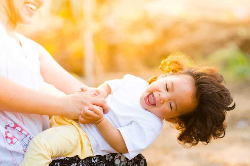 Mother tickling laughing toddler while sitting on their lap to depict the happy side of family time.