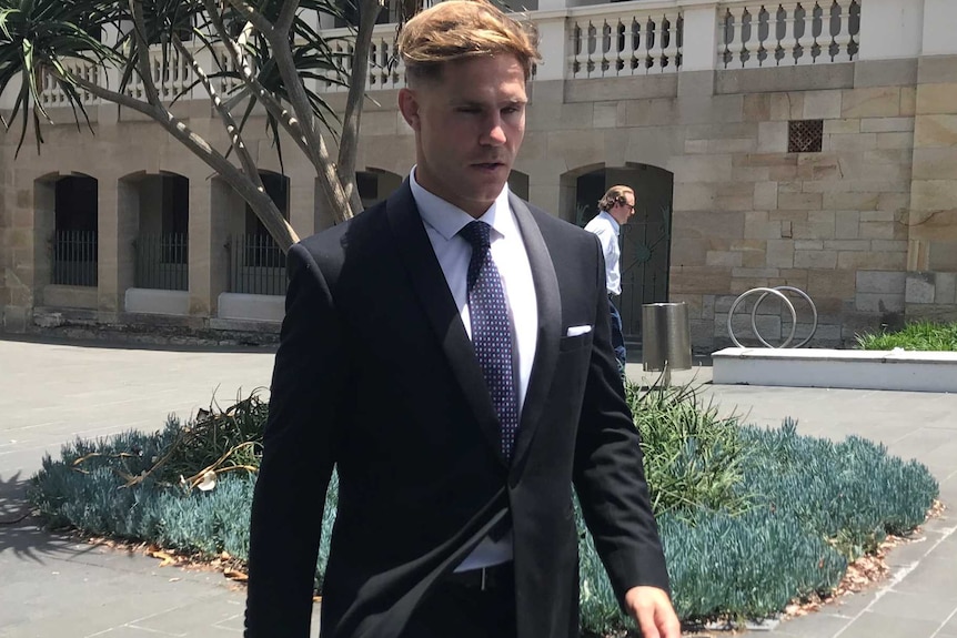 A young man in a dark suit walks away from a court building.