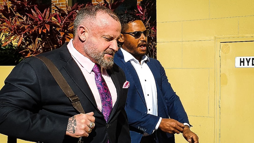 Two men in suits walk past journalists into court.