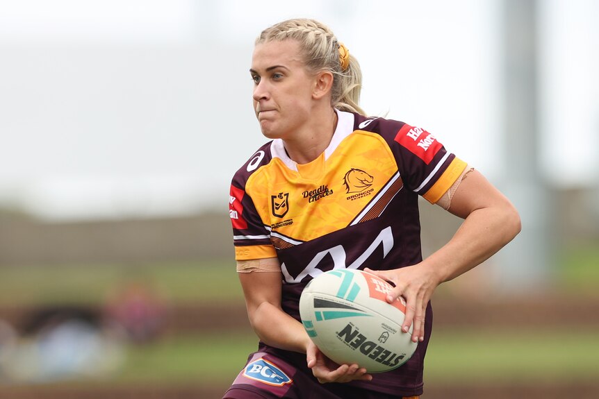 A Brisbane Broncos NRLW player holds the ball as she looks to pass against the Sydney Roosters.
