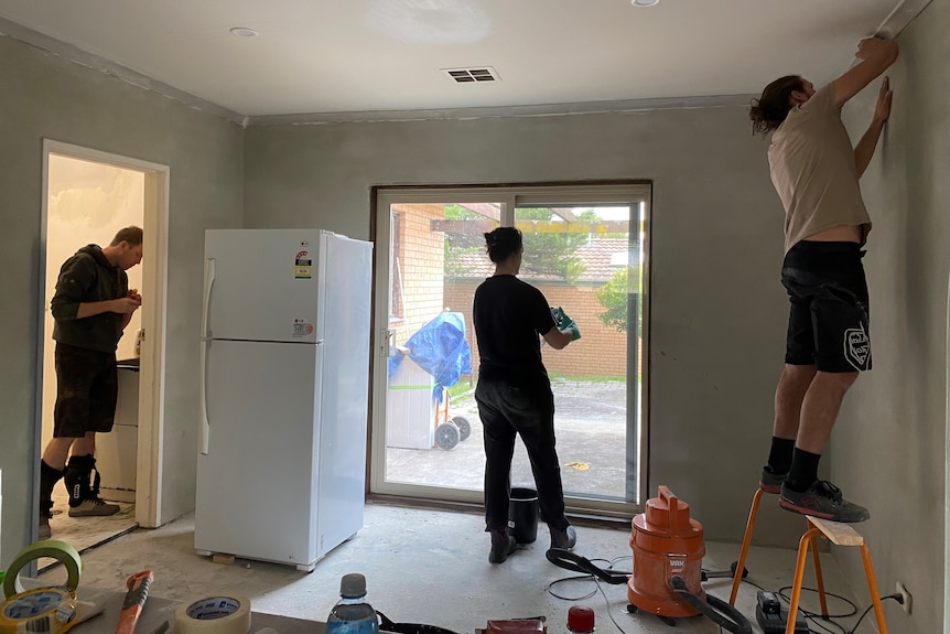 Three people renovating a house with a fridge sitting in the middle of the room