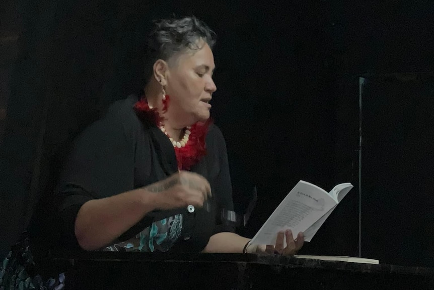 A Samoan woman reading from a book held in her left hand.