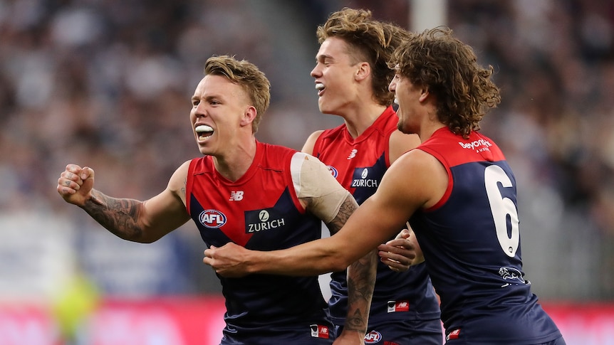 Three Melbourne AFL players embrace as they celebrate a goal.