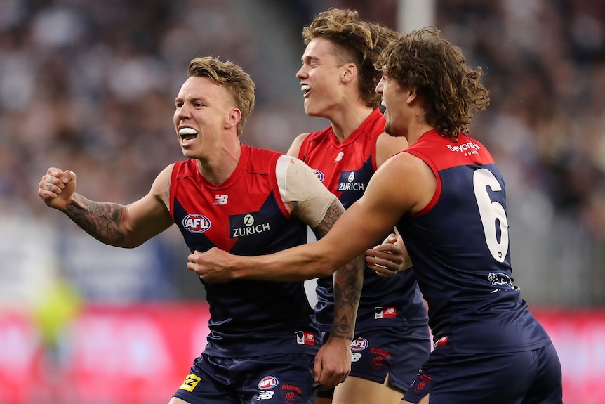 Three Melbourne AFL players embrace as they celebrate a goal.