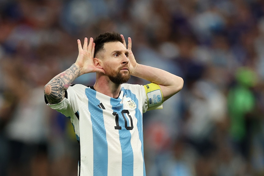 A football player puts his hands up to his ears and signals to the crowd