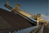 Heavy machinery sits above a large pile of coal at  a mine.