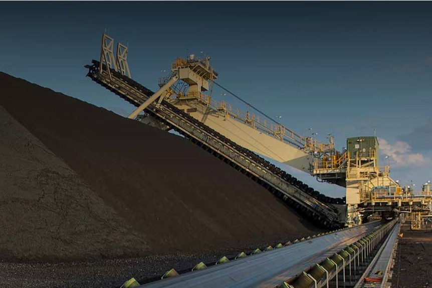 Heavy machinery sits above a large pile of coal at a mine.