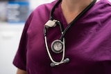 A female doctor carrying a stethoscope., wearing purple scrubs.