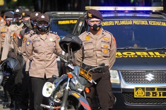 A group of police in Indonesia with a car saying hunters of health protocol offenders.