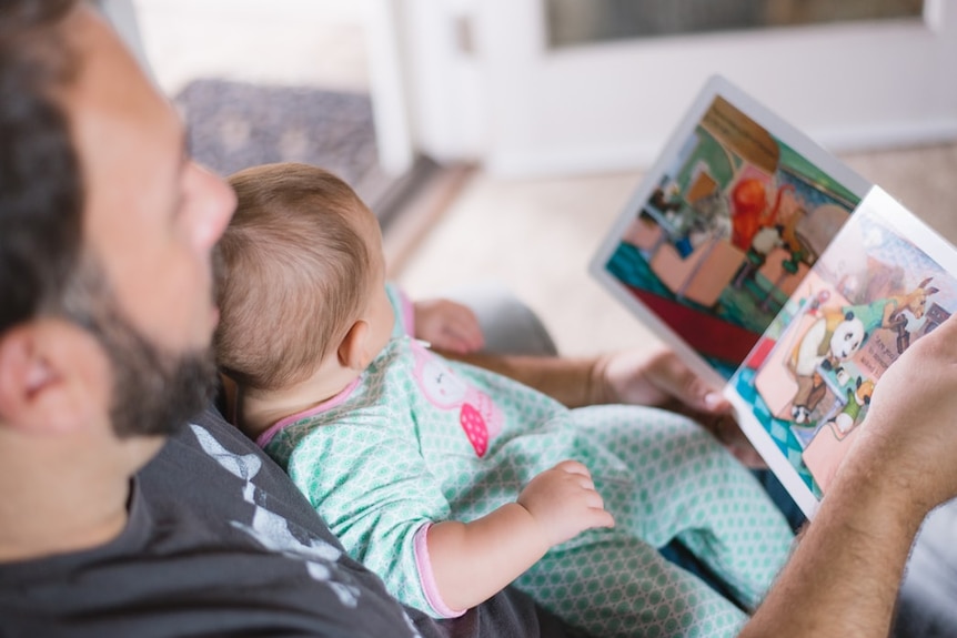 A father reads a book to his young child, who sits on his lap.