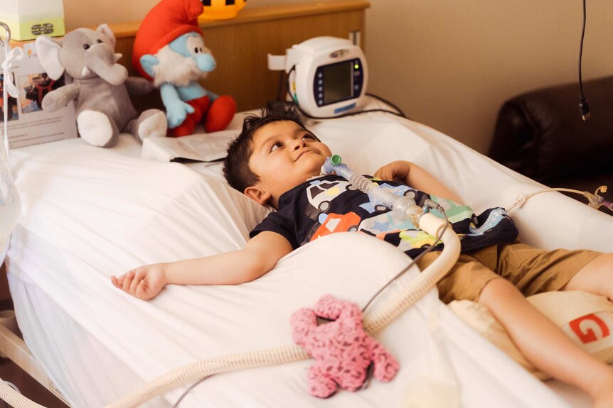 Five-year-old Shaffan Ghulam Muhammad lies on a bed, surrounded by medical equipment and a couple of soft toys.