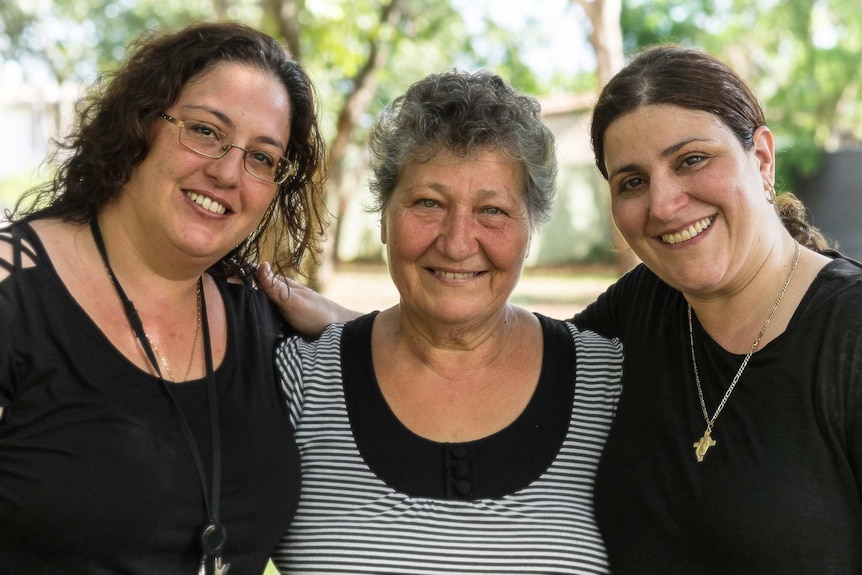 An elderly woman with her two daughters on either side smiling at a camera.