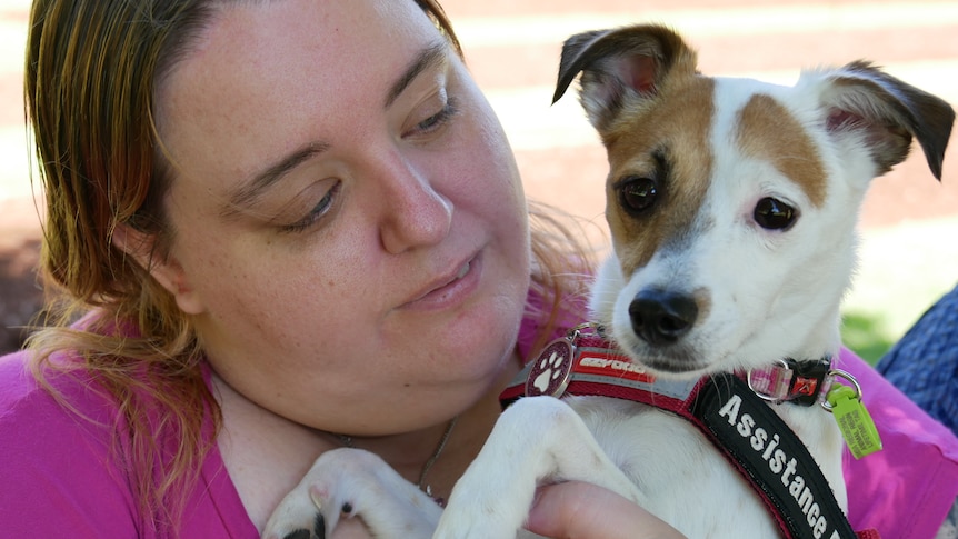 A woman in a pink shirt holds a little white and brown dog. 