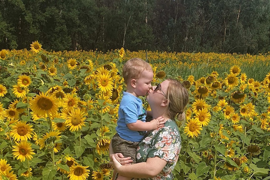 woman holds toddler in field of sunflowers