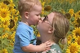 woman holds toddler in field of sunflowers