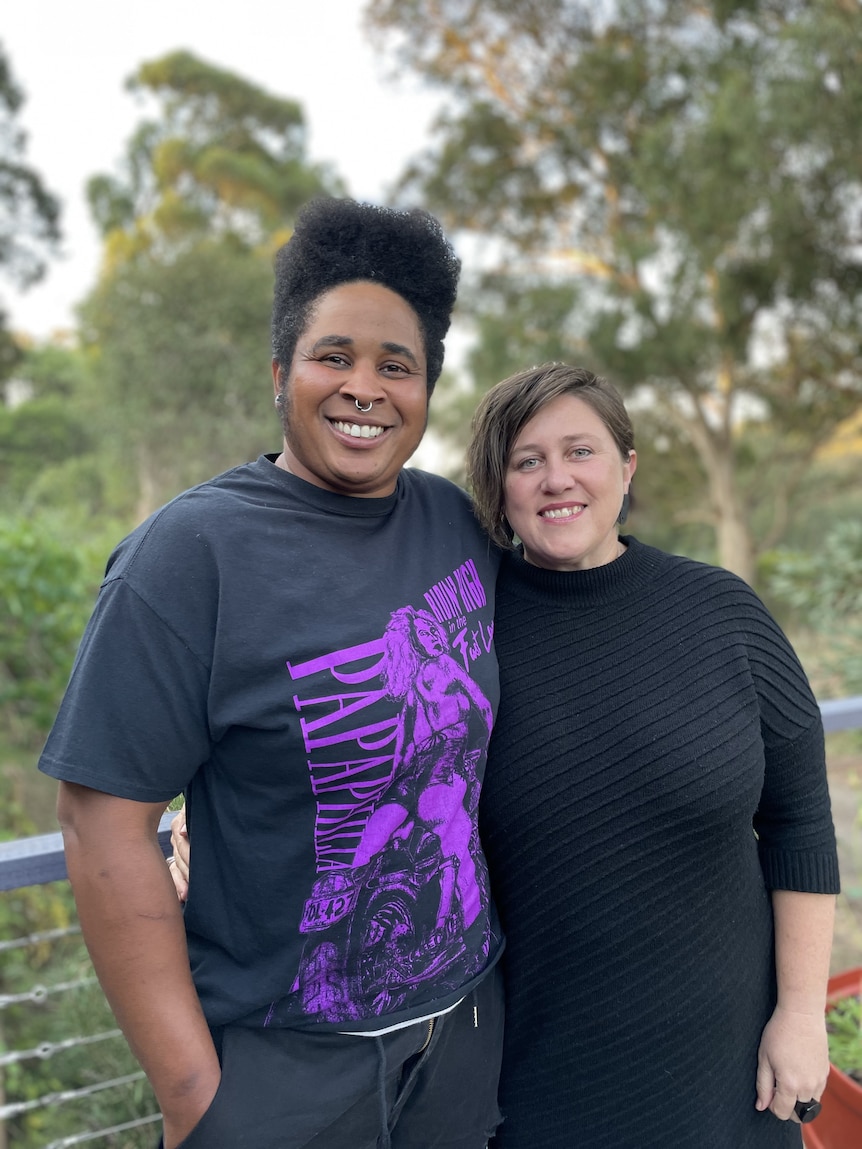 Two women standing arm in arm, smiling in a forest setting