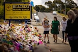 A Hillcrest Primary School sign with hundreds of bunches of flowers arranged on the ground nearby, a