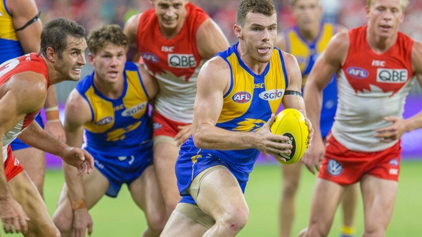 West Coast's Luke Shuey carries the ball while running away from a pack of Sydney Swans players and teammates.