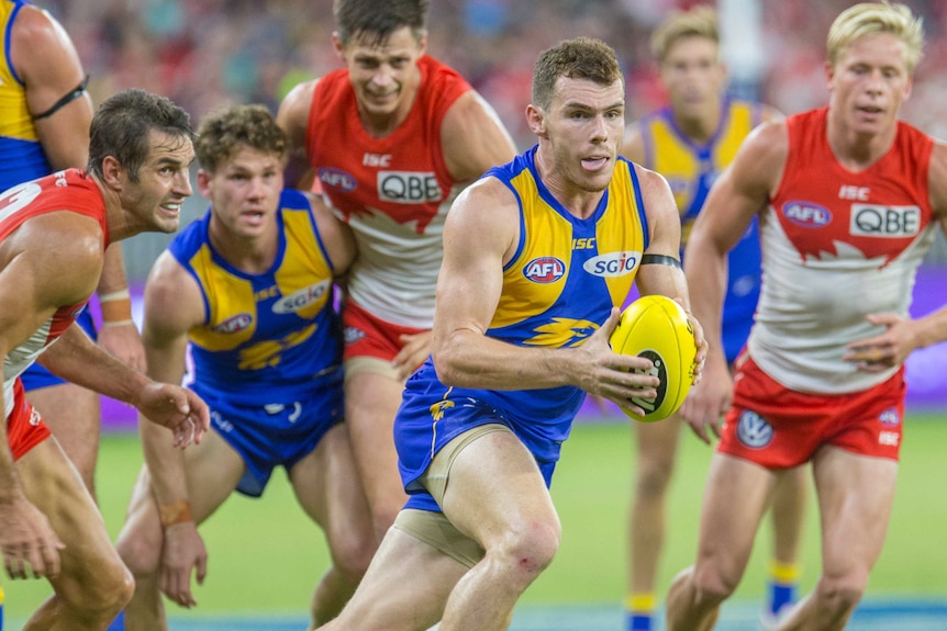 West Coast's Luke Shuey carries the ball while running away from a pack of Sydney Swans players and teammates.