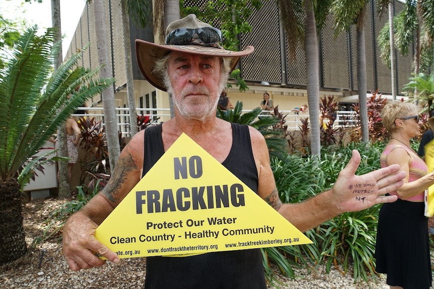A man holds a placard that says "No fracking, protect our water, clean country — healthy community"
