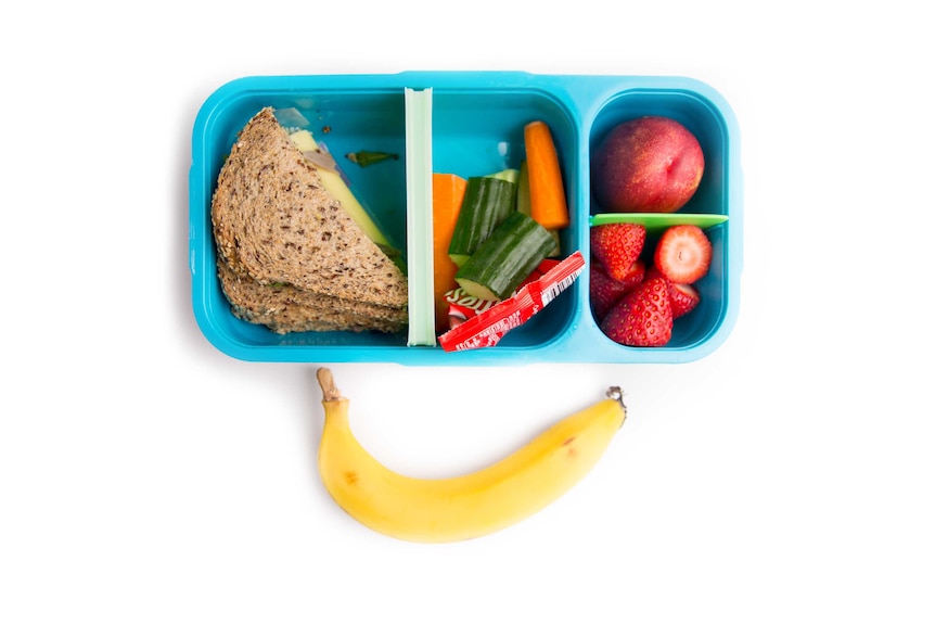 Roast beef multigrain sandwich, carrot and cucumber, a nectarine, strawberries, banana and Maltesers in a blue lunch box.