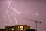 Lighting strikes over the top of a residential unit block with a crane nearby.