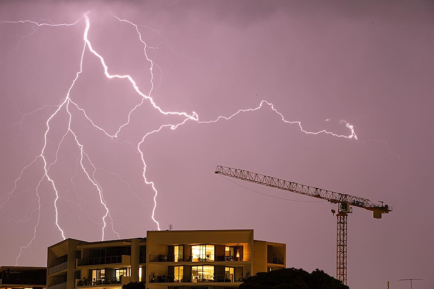 Lighting strikes over the top of a residential unit block with a crane nearby.