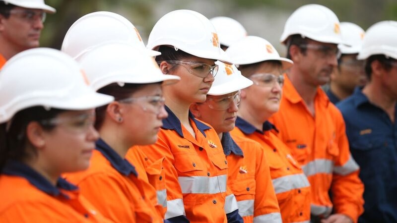 Workers wearing high vis and white hard hats gather and look to the right.