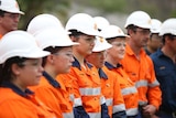 Workers wearing high vis and white hard hats gather and look to the right.