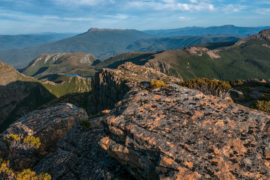 Sunlight bathed rugged rocky outcrops and bush-covered mountains stretch to the horizon