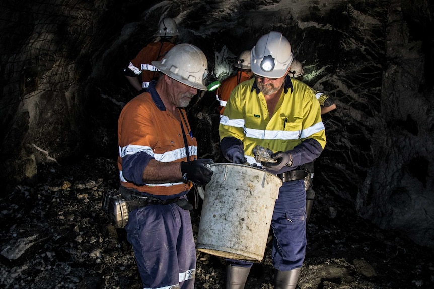 Two mine workers standing next to each other having a discussion in an underground gold mine.