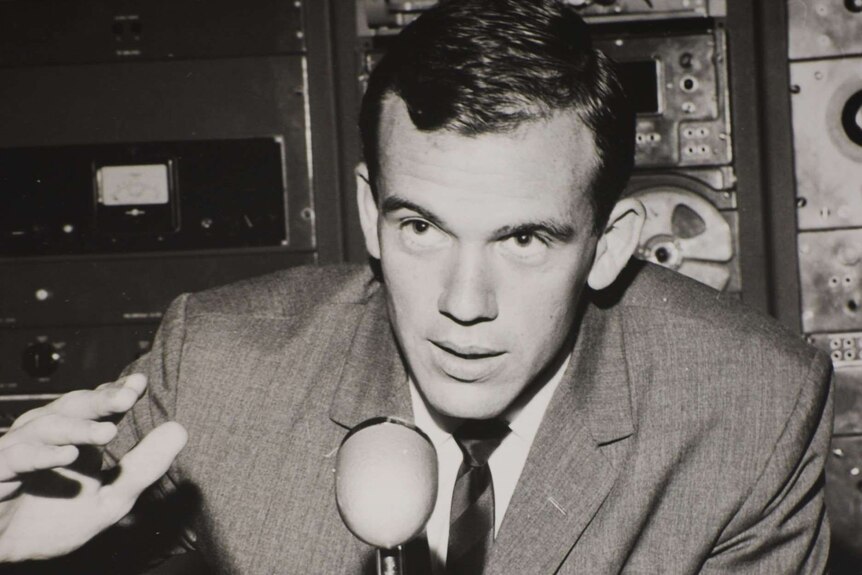 A black and white photo of Mike Willesee in front of a microphone and recording equipment