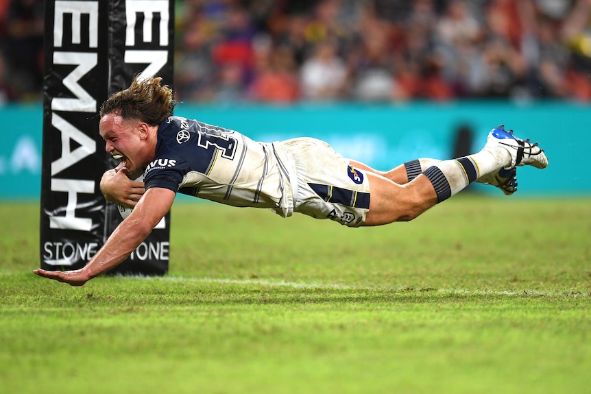 An NRL player flies through the air as he shouts in triumph while about to touch down for a try.