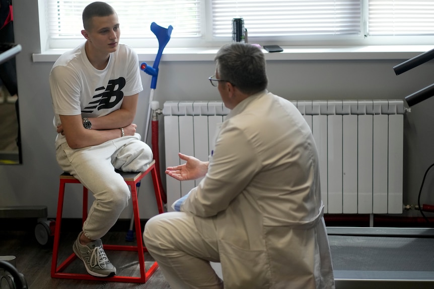 An amputated ukrainian soldier sitting in a clinic with doctors next to him