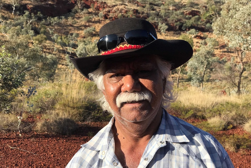 An older Indigenous man standing in the desert. 