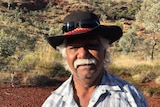 An older Indigenous man standing in the desert. 