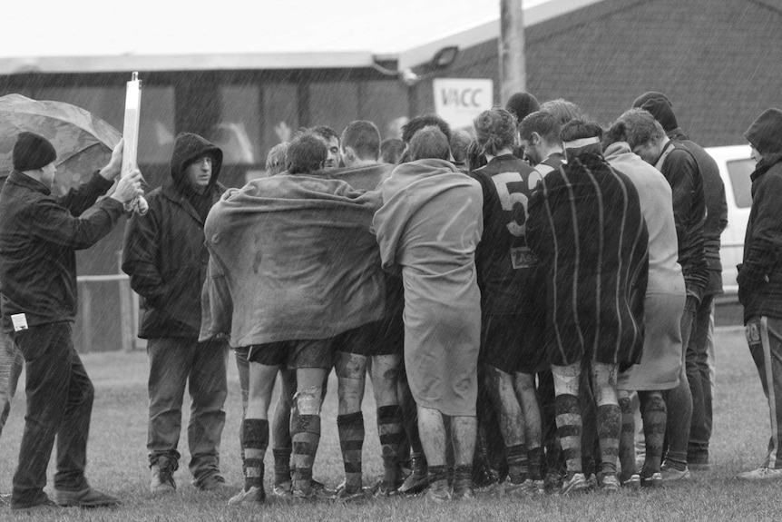 Mirboo North Football Netball Club's senior football team huddle for warmth during a quarter time break.