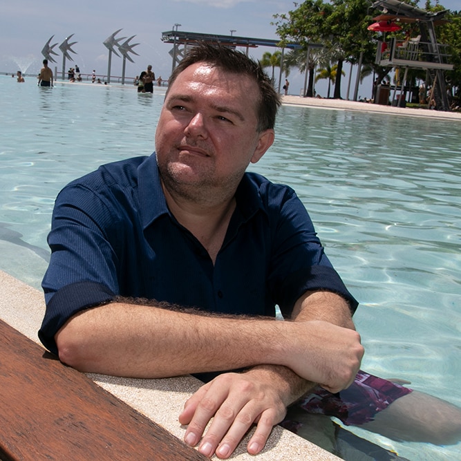 A man with short dark hair, wearing a navy shirt, sitting in a pool.