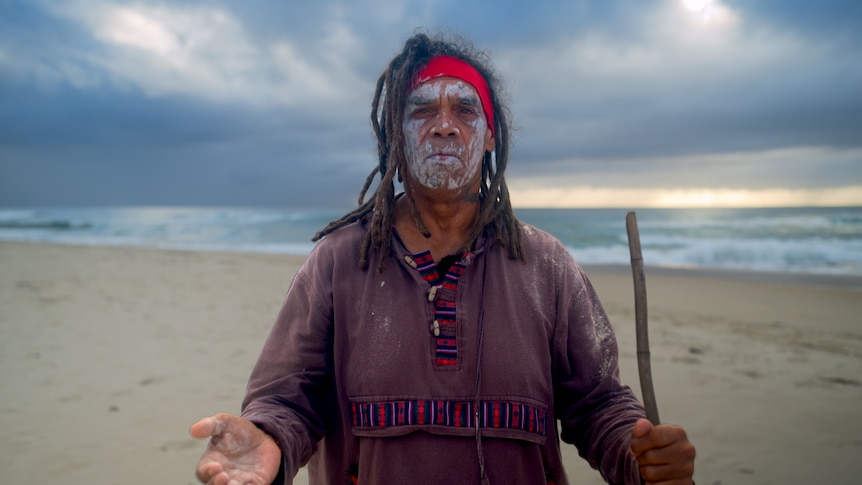 An Indigenous man stands on a beach