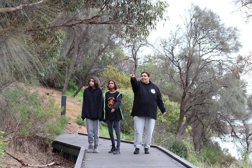 An Indigenous woman and two young girls on a boardwalk in bushland.