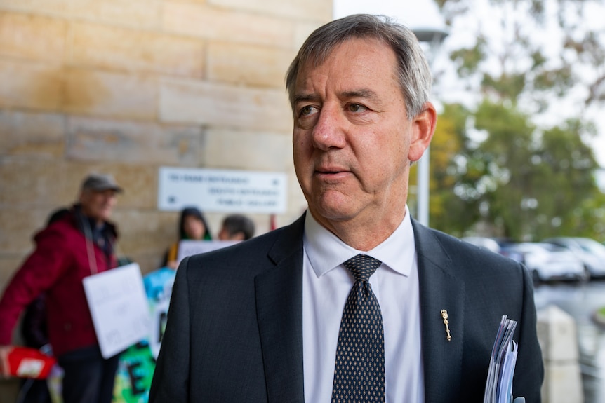 A man in a dark suit stands outside.