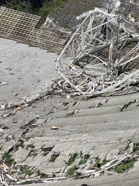 You view an aerial image of a crumpled metal sheet with the damaged arms of a telescope lying on it.