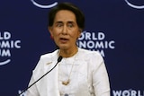 Aung San Suu Kyi sitting in a white chair at a microphone with the World Economic Forum logo behind her.