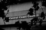 A black and white photo of the Central Coast Council sign with leaves blocking parts of it