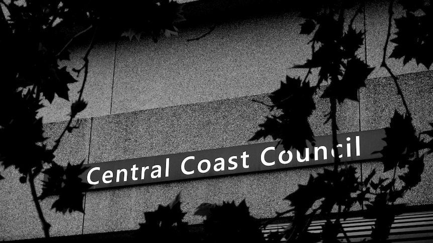 A black and white photo of the Central Coast Council sign with leaves blocking parts of it.